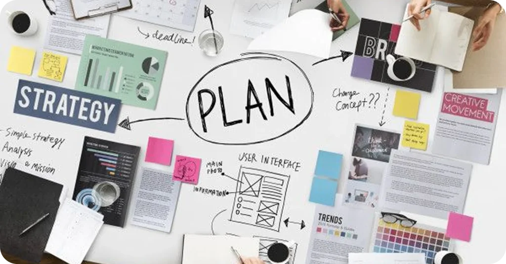 Digital marketing and branding planning workspace with strategy boards, sticky notes, charts, UI wireframes, and creative concepts laid out on a desk during a collaborative planning session.