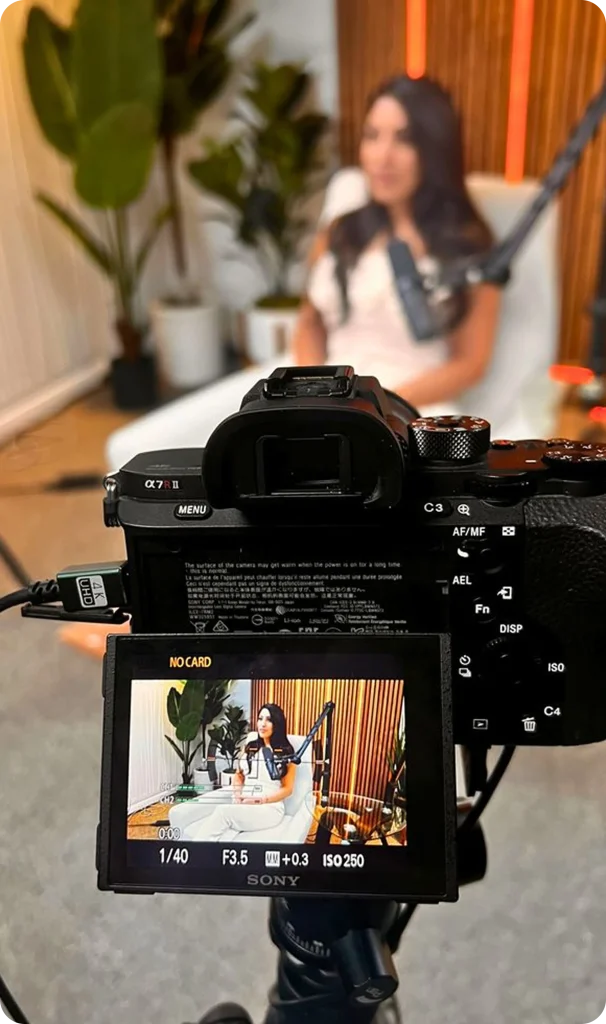Professional camera recording a woman speaking into a podcast microphone in a modern studio, with the camera screen showing a framed interview shot, representing podcast production, video content creation, and digital media recording.