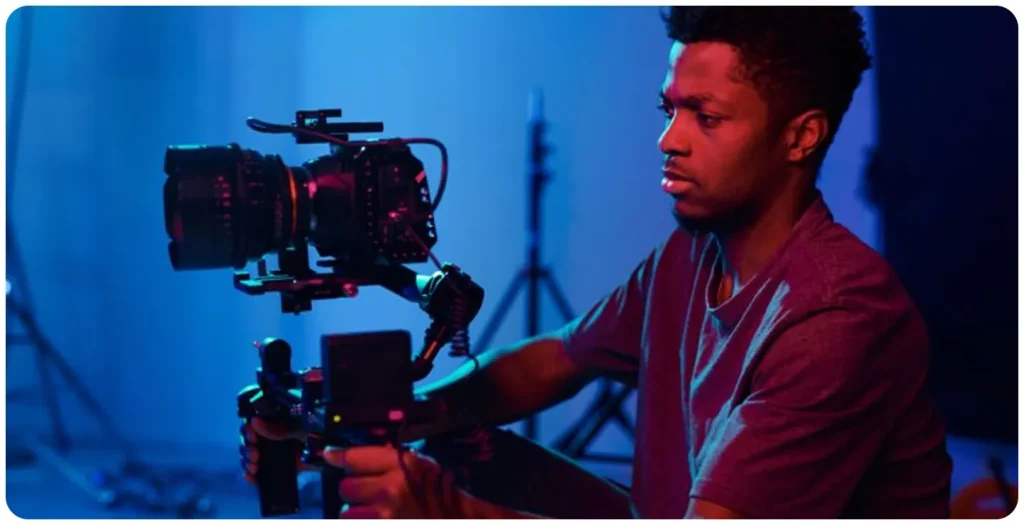 Videographer operating a professional cinema camera mounted on a stabilizer, working in a studio with blue and red lighting.